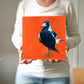 photo of a woman holding an oil painting on panel closeup of the head of a magpie in blue with a bright orange background